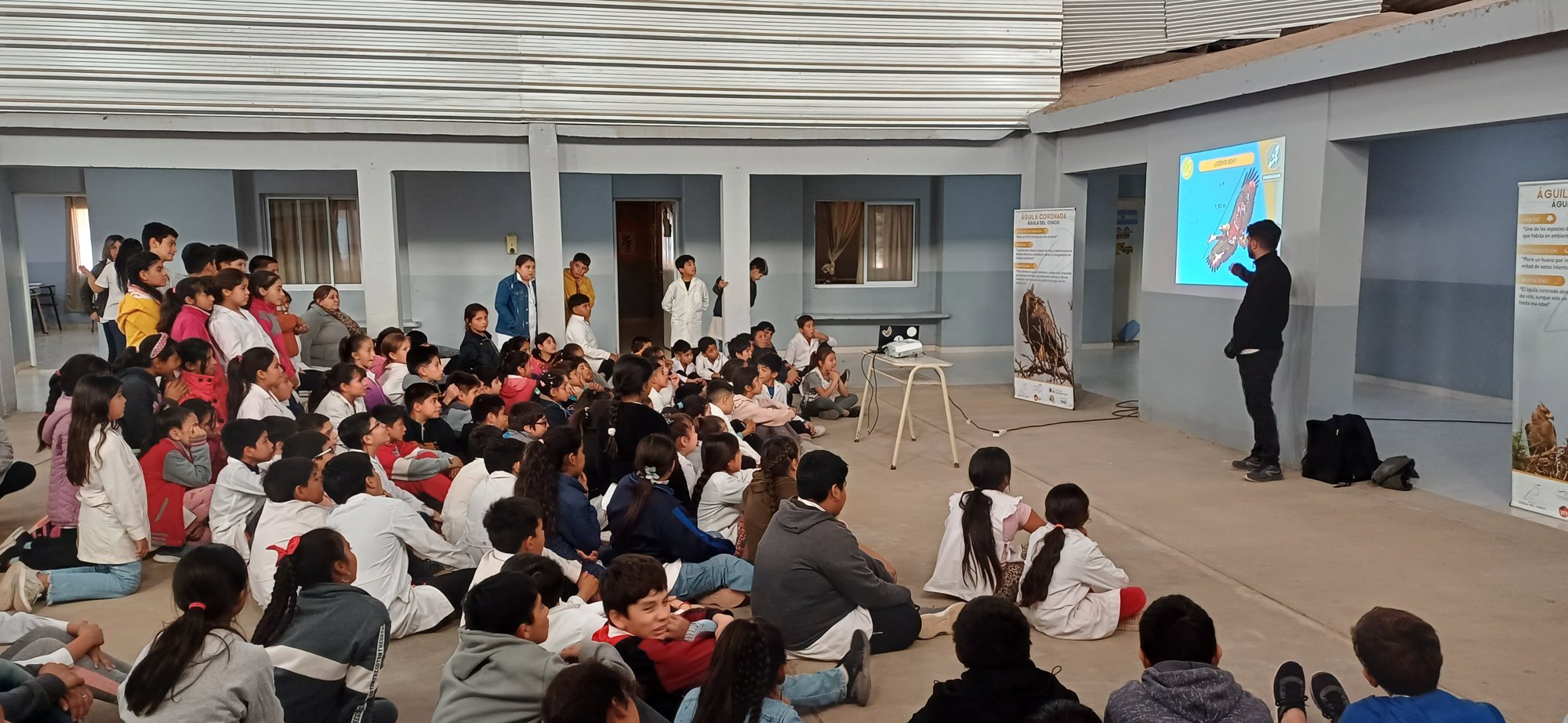 Charla sobre el águila coronada o del Chaco en una escuela, con estudiantes sentados frente a la proyección